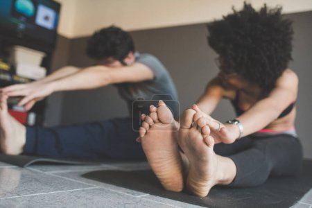 Téléchargez les photos : Couple multiethnique à la maison pratiquant le sport faire du yoga fitness - en image libre de droit