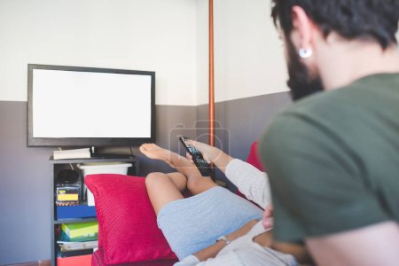 Téléchargez les photos : Jeune couple multiethnique à l'intérieur appartement assis canapé regarder la télévision - en image libre de droit