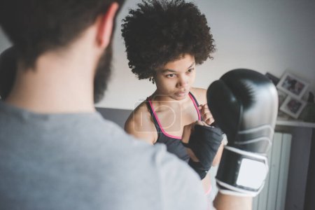 Foto de Mujer joven multiétnica en el entrenamiento en casa con entrenador haciendo ejercicio de boxeo - Imagen libre de derechos
