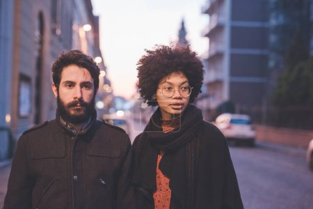 Téléchargez les photos : Jeune couple multiethnique marchant à l'extérieur des rues de la ville la nuit - en image libre de droit
