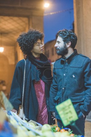 Téléchargez les photos : Jeune couple multiethnique en plein air ville achat de légumes et fruits épicerie - en image libre de droit