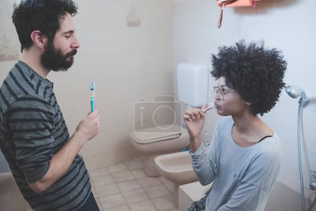 Téléchargez les photos : Jeune couple multiethnique salle de bain intérieure brossage des dents - en image libre de droit