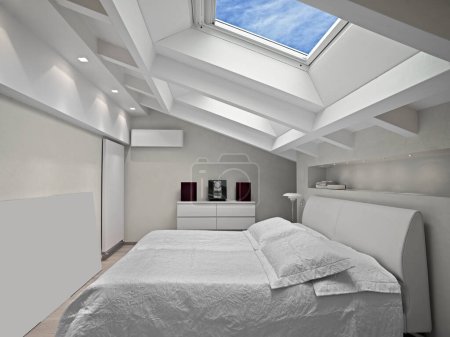 Innenaufnahmen eines modernen Schlafzimmers in der Mansarde im Vordergrund das Bett und das Dachfenster