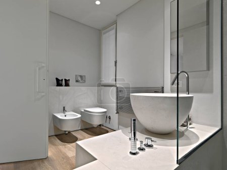 Moderne Badausstattung im Vordergrund die Arbeitsplatte Waschbecken im Hintergrund gibt es ein Bidet und WC-Schüssel der Boden ist aus Holz