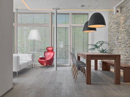 Téléchargez les photos : Interior of the modern living room on the right there is a dining table with its chairs while on the left there is a sofa and a red armchair the floor is wooden - en image libre de droit