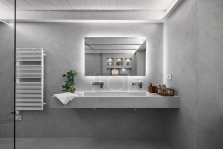 Foto de Vista interior de un baño moderno, en primer plano está el lavabo de encimera en la parte superior de mampostería, todas las paredes y el suelo están cubiertos de resina gris - Imagen libre de derechos