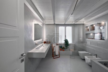 Téléchargez les photos : Vue intérieure d'une salle de bain moderne revêtue de résine grise avec plafond en bois, au premier plan, à gauche, l'évier intégré et au-dessus il y a un grand miroir rectangulaire - en image libre de droit