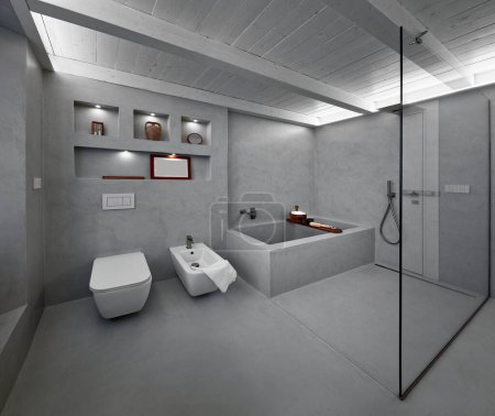 Téléchargez les photos : Salle de bain moderne intérieur recouvert de résine grise avec baignoire et douche en maçonnerie, un mur de verre sépare leur de l'entrée doo - en image libre de droit