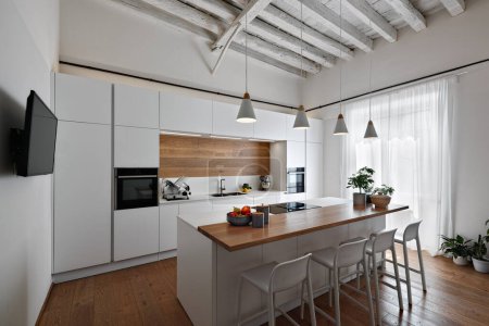 Téléchargez les photos : Vue d'un intérieur d'une cuisine moderne au premier plan la cuisine de l'île avec plateau en bois et quatre tabourets, au-dessus quatre lampes suspendues, le sol et le plafond sont en bois - en image libre de droit