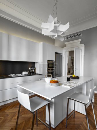 Téléchargez les photos : Vue intérieure d'une cuisine blanche moderne au premier plan l'îlot de cuisine avec deux tabourets, l'éclairage est confié à une lampe suspendue le sol est en bois - en image libre de droit