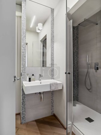 Foto de Interior de un moderno cuarto de baño con suelo de madera en primer plano el lavabo con un espejo a la derecha hay una caja de ducha de mampostería - Imagen libre de derechos