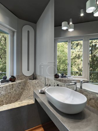 Foto de Interior de un cuarto de baño moderno, en primer plano el lavabo de la encimera en la parte superior de mampostería en lugar en el fondo en la esquina debajo de la ventana hay una bañera de mampostería - Imagen libre de derechos