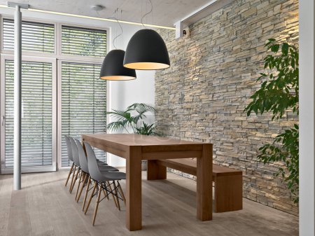 Foto de Interior de la moderna sala de estar en primer plano hay una mesa de comedor detrás de la cual hay una pared de piedra, el piso está hecho de madera - Imagen libre de derechos