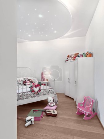 Téléchargez les photos : Interior of a modern children's bedroom with a parquet floor and some toys and puppets scattered on the bed and on the floor - en image libre de droit