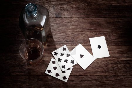 Juegos de azar del viejo oeste. Mano de hombre muerto. Mano de póquer de dos pares compuesta por ases negros y ochos negros con botella de licor y vaso de whisky.