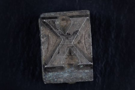 Antiker beweglicher Buchstabe X auf schwarzem Hintergrund.