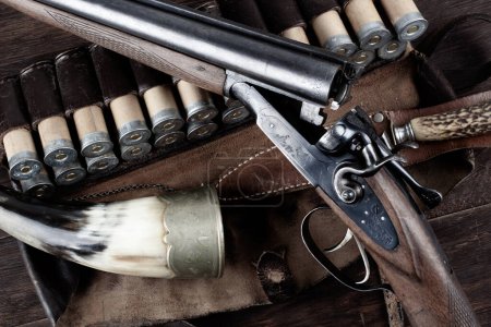 fusil de chasse latéral à double canon avec cartouches en bandolier sur table en bois.
