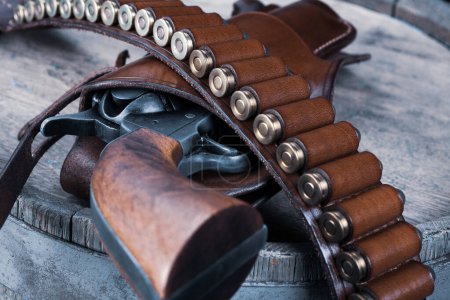 Old west gun with belt, holster and ammunition on wooden barrel