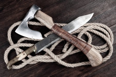 small axe with bowie knife and rope on wooden background