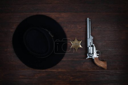 Old west gun, marshal star and black hat on table. Top view.
