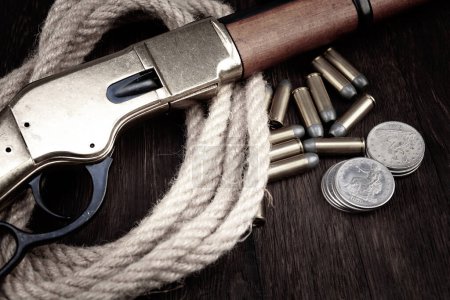 Old west lever action repeating rifle with ammunition and silver dollar coins on wooden table.