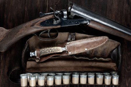 fusil de chasse latéral à double canon avec cartouches en bandolier sur table en bois.