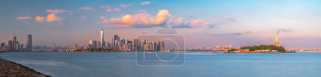 Foto de Nueva York, Nueva York, Estados Unidos skyline desde el puerto con Ellis Island y la Estatua de la Libertad al atardecer. - Imagen libre de derechos