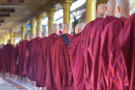 Foto de BAGO, MYANMAR - 19 DE OCTUBRE DE 2015: Los monjes hacen cola para recibir ofrendas de comida a la hora del almuerzo en el Monasterio Kyaly Khat Wai
. - Imagen libre de derechos