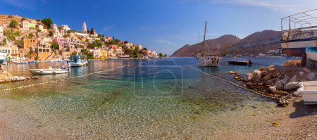 Hillside panoramic view of the colorful buildings and busy harbor on Symi Island, Greece.