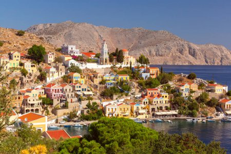 Wide panoramic shot of Symi Island with colorful houses against scenic mountain backdrop, Greece
