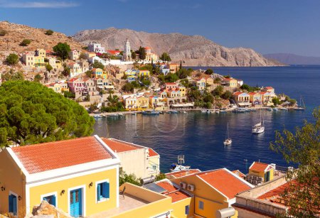 Wide panoramic shot of Symi Island with colorful houses against scenic mountain backdrop, Greece