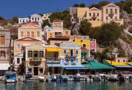 Hillside view of the colorful buildings and busy harbor on Symi Island, Greece.