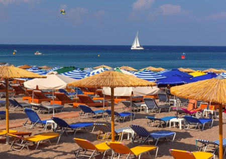 Colorful beach scene in Rhodes, Greece, with loungers and sailing boat