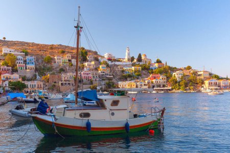 Blick auf bunte Häuser und Boote im Hafen der Insel Symi, Griechenland, bei Sonnenuntergang