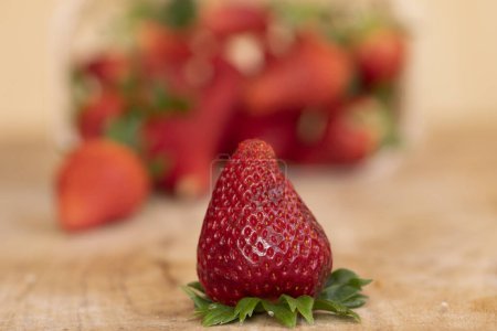 Téléchargez les photos : Fraise mûre devant un panier d'autres fraises sur une table en bois - en image libre de droit