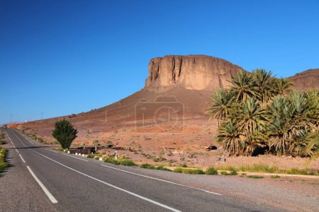 Morocco desert road in Anti-Atlas mountains. Ouarzazate Province landscape with rock island. Palm tree oasis.