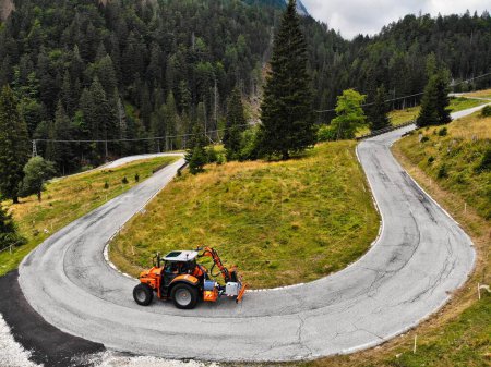 Foto de Italia vista del dron. Passo di Pramollo (Nassfeld Pass) sinuoso camino de montaña con tractor trabajador de mantenimiento. - Imagen libre de derechos