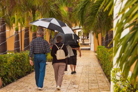 Foto de Turistas ancianos bajo la lluvia en el callejón del hotel dando un paseo, Tulum, México - Imagen libre de derechos