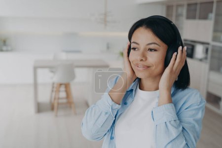 Mujer feliz usando auriculares inalámbricos escuchando música, podcast o audio libro, disfrutando de una calidad de sonido perfecta. Sonriente mujer tranquila escuchar afirmaciones positivas en los auriculares, relajarse en casa.