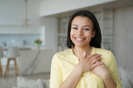 Photo for Thankful smiling peaceful woman keep hands close to heart, feeling gratefulness, appreciation, hope, standing alone at home. Emotional young female expressing deep gratitude, happy with good deed. - Royalty Free Image
