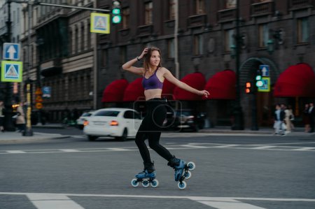 Photo for Outdoor shot of sim woman rides on rollerblades loks away trains different muscle groups of legs and core develops endurance manages her weight burns calories improves balancing. Cardio workout - Royalty Free Image