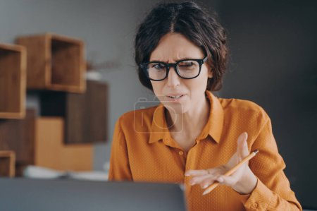 Photo for Negative emotions at work. Frustrated Spanish female freelancer looking angry on laptop screen doesnt understand error in calculations came out while checking sales reports and documentations online - Royalty Free Image