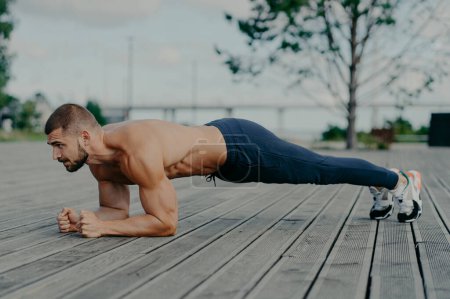Photo for Motivated male athlete does abs exercise, enjoys bodybuilding training outdoor and stands in plank. Strong muscular European adult man has fitness workout. People and healthy lifestyle concept - Royalty Free Image