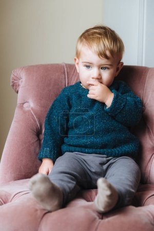 Photo for Thoughtful little child sits on comfortable armchair, thinks about something, feels bored alone, waits for parents, going to have breakfast or go to kindergarten. Pensive small boy in trendy clothes - Royalty Free Image