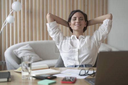 Photo for Positive Spanish woman rests during remote work online at home. Freelance lady sitting in front of laptop in relaxed position with satisfied smile on her face while eyes closed and hands behind head - Royalty Free Image