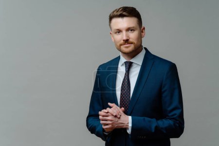 Formal style. Serious bearded male entrepreneur keeps hands together wears formal clothes dressed in office attire poses against grey background with copy space for your promotional content.