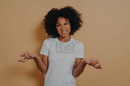 Photo for I dont know. Studio shot of confused young african female can not make decision, shrugging shoulders and does not know what happened, dressed in white t shirt feeling embarrassed. Doubtfulness concept - Royalty Free Image