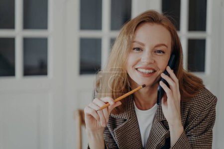 Photo for Positive mid adult businesswoman is working from home and having phone call. Attractive emotional european lady is freelancer, entrepreneur or accountant. Smiling happy woman works distantly. - Royalty Free Image