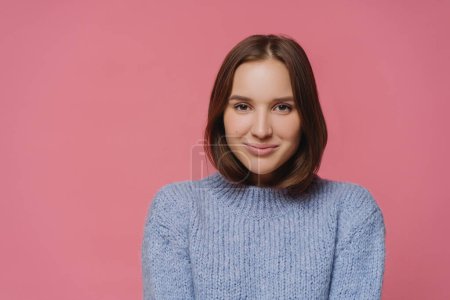 Photo for Beautiful brunette lady in knitted warm sweater looks directly at camera, smiles positively, enjoys nice winter day, isolated over pink background, has pleasant conversation with interlocutor - Royalty Free Image