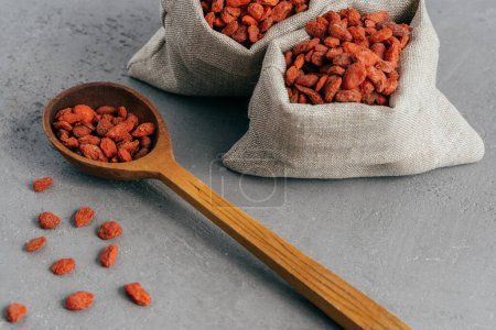 Photo for Wolfberries in small cloth sacks and wooden spoon, spread on grey background. Red goji fruit. Whole foods. Healthy diet concept - Royalty Free Image